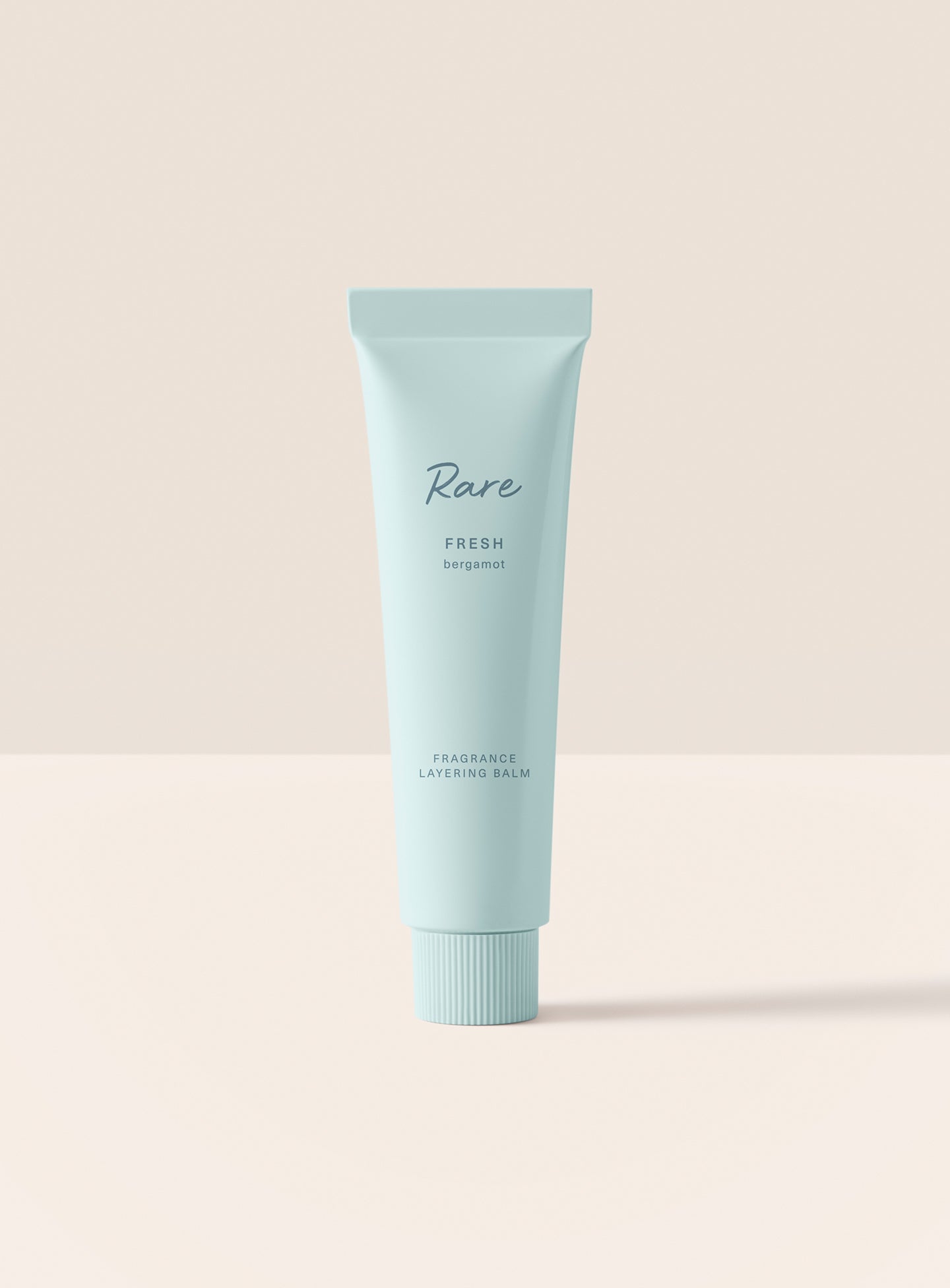 The Rare Fresh Bergamot Fragrance Layering Balm stands upright in its minimalist green packaging.